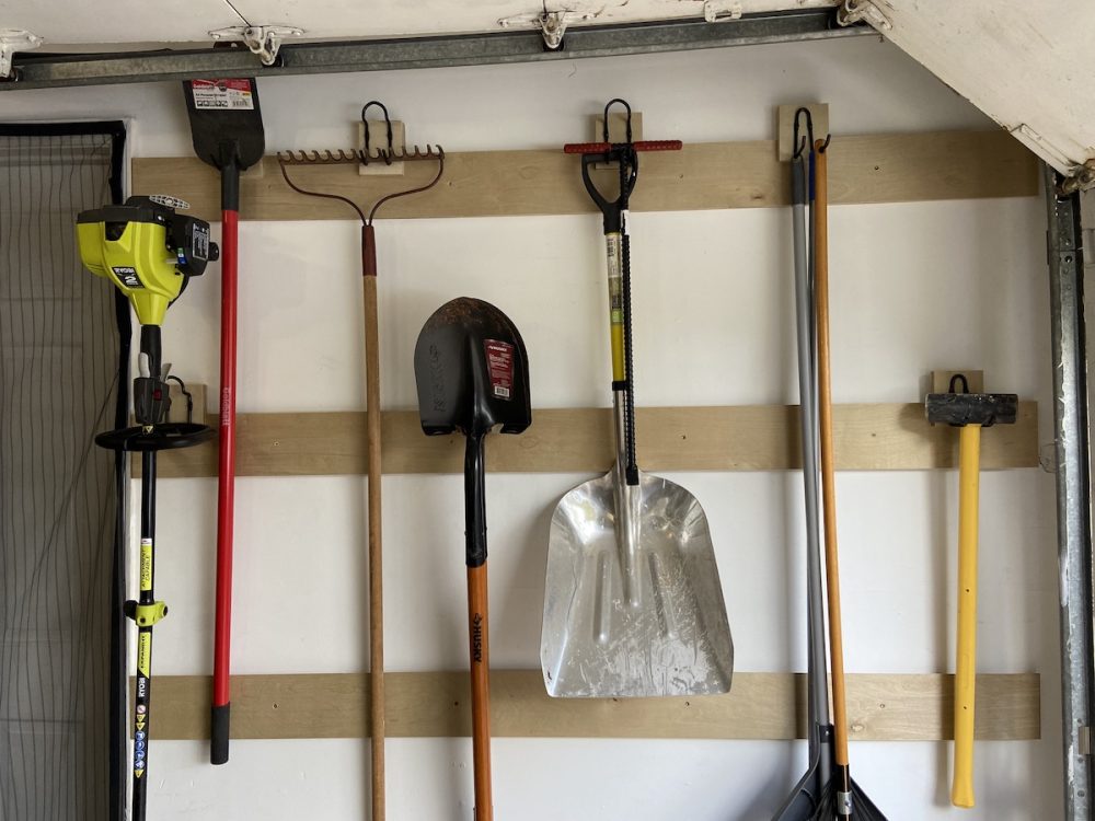 Shovels, rake and other garden tools hanging from wooden cleat rails in a garage